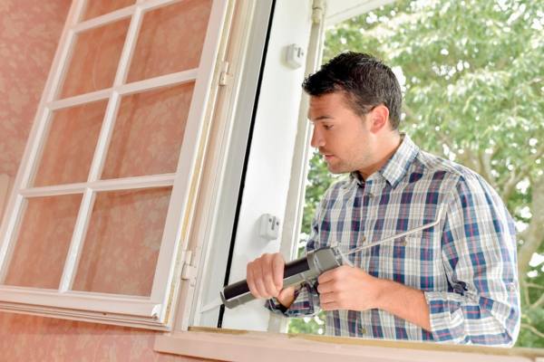 man putting sealant on window