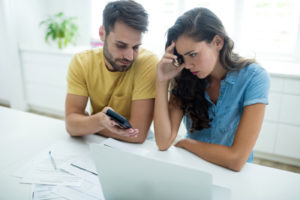 Worried couple calculating their air conditioner repair costs with laptop in the kitchen