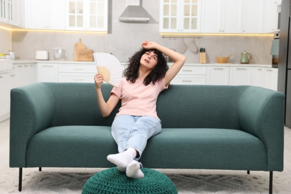 woman feeling warm indoors using hand fan to cool herself