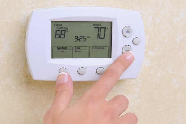 image of person adjusting thermostat to turn on furnace