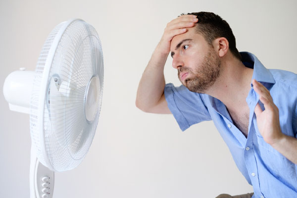 man cooling himself with a fan due to an air conditioner that wont turn on