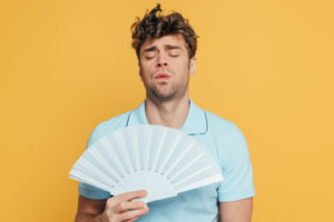 man cooling himself with a fan due to high humidity levels at home and ac short cycling