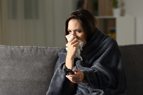 image of homeowner sneezing under blanket depicting air quality in winter