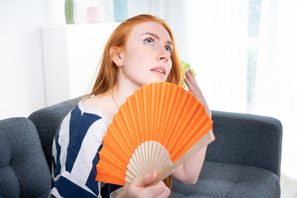 woman suffering from heat using hand fan due to AC breakdown