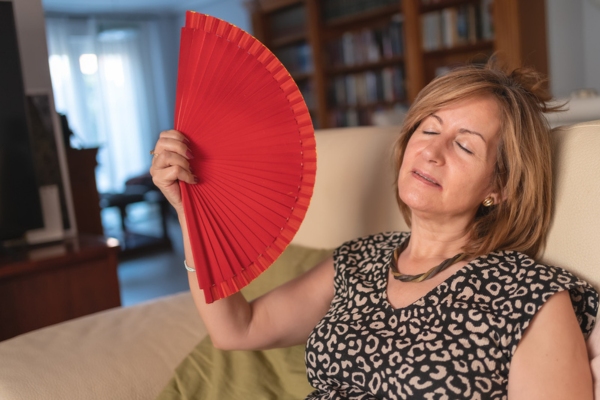 woman using hand fan due to heat pump blowing hot air instead of cool