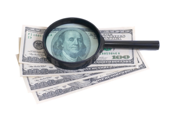 magnifying glass on top of dollar bills depicting evaluating costs