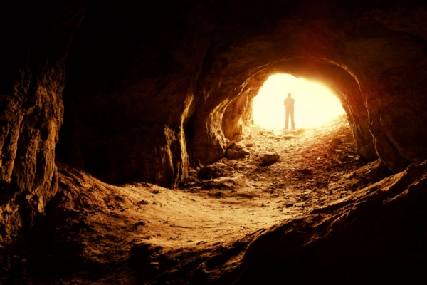 silhouette of a man standing in front of a cave entrance