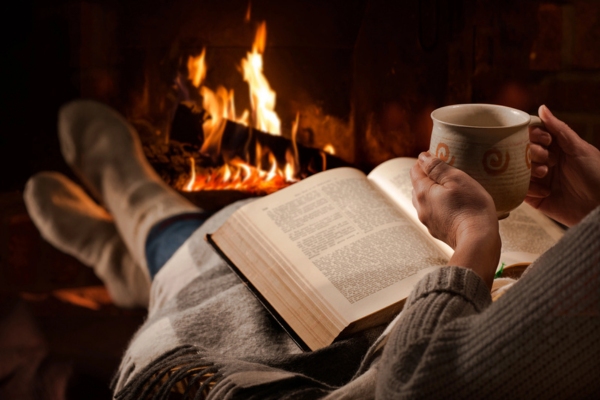 woman reading a book and drinking coffee in front of the fireplace