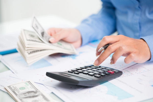 close up of a man's hand counting money and using a calculator depicting heating oil prices