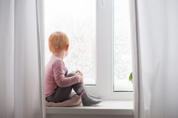 red haired child looking out the window during winter