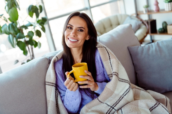 woman drinking coffee on the couch feeling cozy depicting Heating & Cold Weather Performance