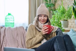 woman keeping warm during winter while drinking coffee on the couch