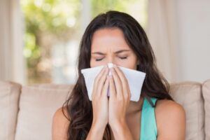 image of a woman covering nose while sneezing due to allergies caused by pollen indoors