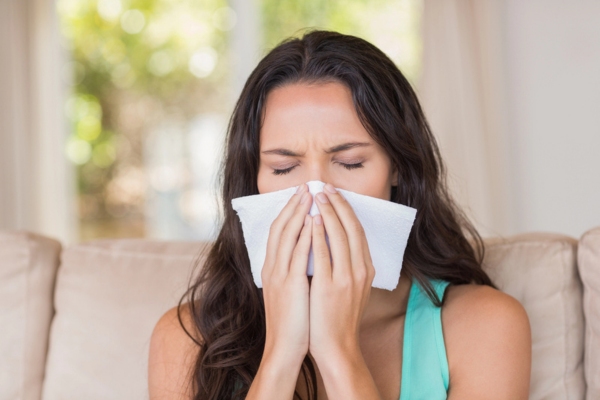 image of a woman covering nose while sneezing due to allergies caused by pollen indoors