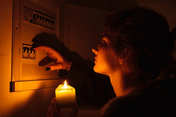 Young woman holding a candle in complete darkness examining electricity box due to power outage