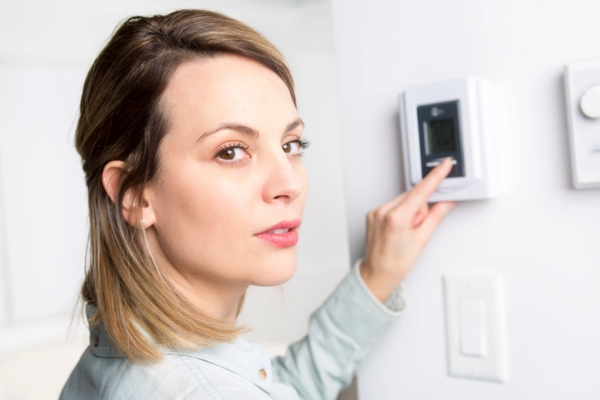 woman setting up home thermostat to lower temperature overworking AC