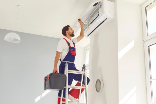 HVAC technician on a ladder inspecting modern ductless air conditioner